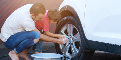 Mann und Kind waschen draußen vor der Garage ein Auto