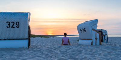Eine Frau sitzt bei Sonnenuntergang zwischen zwei Strandkörben am Strand