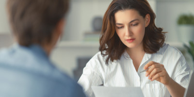 Zwischenzeugnis anfordern: Haben Arbeitnehmer Anspruch darauf? Eine junge Frau mit kurzen Haaren sitzt an einem Büro-Schreibtisch einer älteren Frau gegenüber.