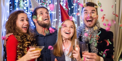 Nachtruhe an Silvester: Das sind die Regeln. Vier junge Männer und Frauen sind feierlich gekleidet. Konfetti regnet auf sie herab.