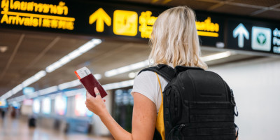 Frau mit Reisepass und Ticket in der Hand unter digitaler Anzeige am Flughafen