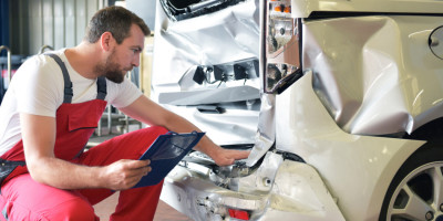 Mann KFZ-Mechaniker in rotem Overall prüft in Werkstatt Schaden an Auto