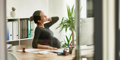 Schwangere Frau sitzt am Schreibtisch in Büro und reibt sich den Nacken