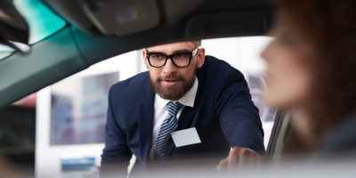 Experienced male sales manager demonstrating features of car when client sitting in vehicle