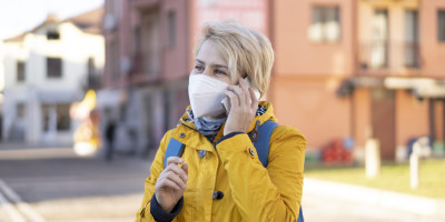 Frau in einen gelben Regenmantel, trägt eine FFP2 Maske