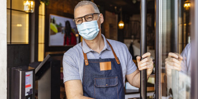 Gastronom mit Maske auf, öffnet seine Restaurant Tür