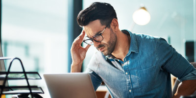 Mann vor Laptop fasst sich frustriert an den Kopf