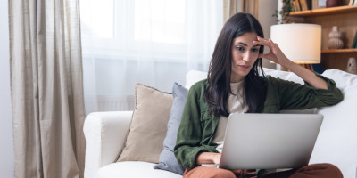 Junge dunkelhaarige Frau sitzt konzentriert mit Laptop auf dem Sofa 
