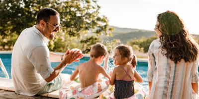 Familie mit zwei Kindern sitzt am Pool und lacht