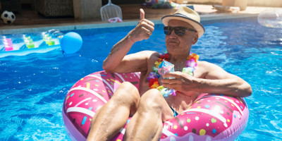 Alter Mann sitzt im Schwimmring im Pool und hebt den Daumen hoch