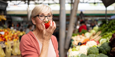 Ältere Frau auf dem Markt hält Tomate vors Gesicht