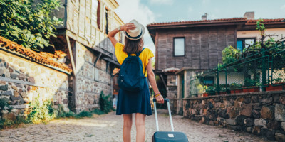 Frau in Sommerkleidung mit Rollkoffer im Urlaub