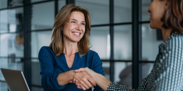 Lachende Frau bei der Arbeit gibt anderer Frau die Hand