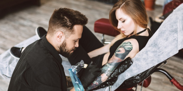 Tattoo Artist sticht Frau im Studio ein Tattoo auf dem Arm