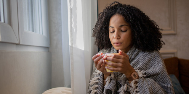 Frau sitzt vor Fenster mit Tasse in der Hand