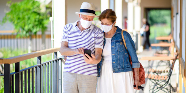 Älteres Paar schaut auf ihr Handy und tragen Masken