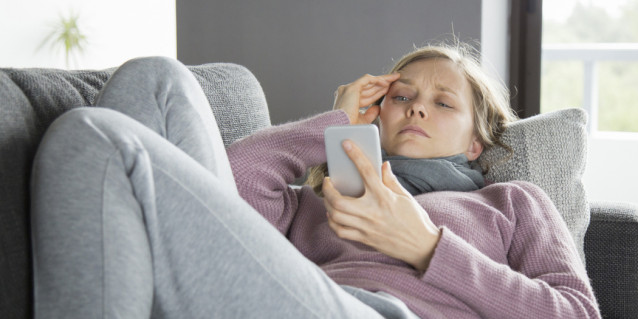 Kranke Frau mit Schal schreibt eine Nachricht am Handy.