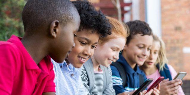 Fünf Schülerinnen und Schüler sitzen draußen und gucken auf Handys
