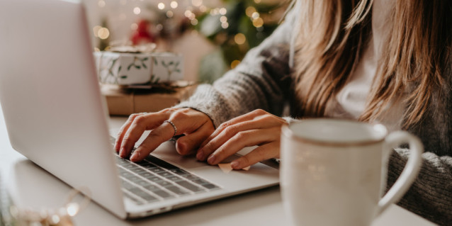 Eine Frau tippt in einen Rechner, eine Kaffeetasse steht auf dem Schreibtisch