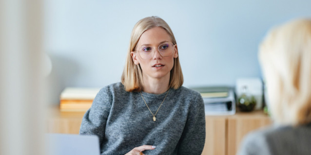 Junge blonde Frau sitzt bei einem Bewerbungsgespräch in einem Büro einer anderen Person gegenüber