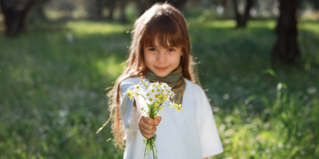 Mädchen steht bei Sonnenschein auf einer Wiese und hält einen Wildblumenstrauß in der Hand