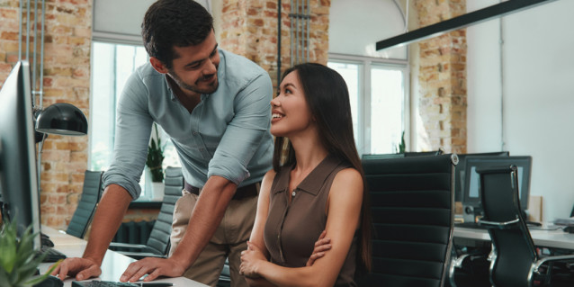 Happy to work with you! Two cheerful young colleagues in casual wear looking at each other with smile and discussing fresh ideas while working together in modern office. Workplace. Business concept.