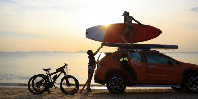 Silhouette couple traveler take paddle board to roof rack of car against sunset sky . Sport activity and lifestyle after workout at beach