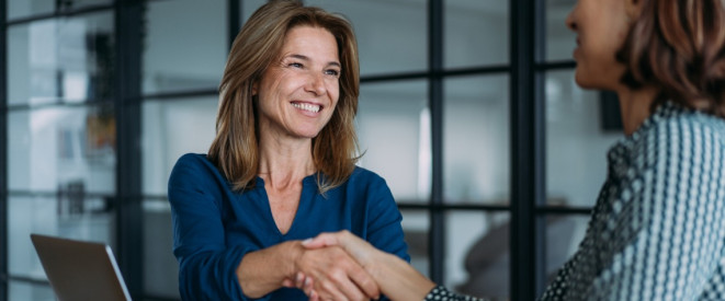 Lachende Frau bei der Arbeit gibt anderer Frau die Hand