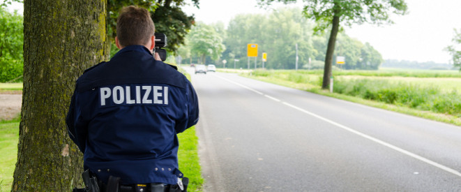 Polizist baut Blitzer hinter einem Baum an der Landstraße auf