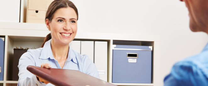 Frau im Büro überreicht dem Mann ihr gegenüber eine Mappe