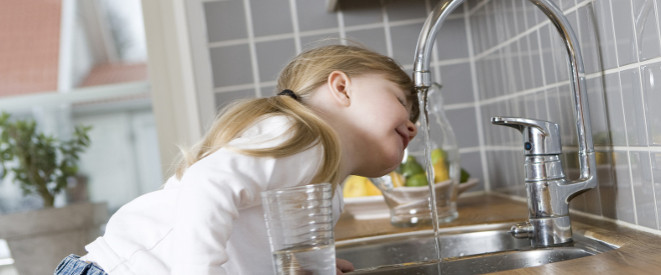 kleines Mädchen lehnt sich in der Küche unter den Wasserhahn zum Trinken