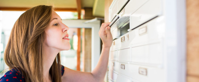 junge Frau schaut in den Briefkasten eines Mehrfamilienhauses