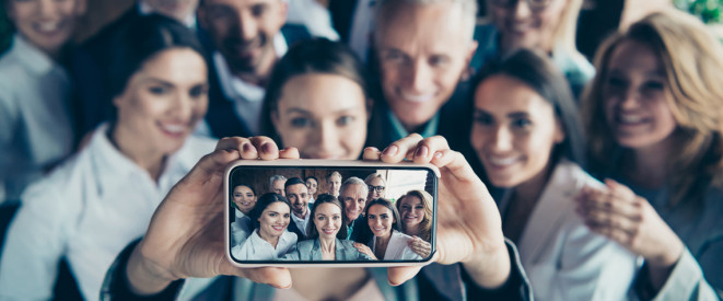 Frau macht Selfie von sich mit Gruppe im Hintergrund