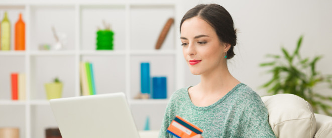 junge Frau mit Kreditkarte in der Hand sitzt vor dem Laptop