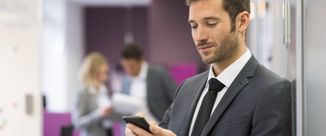 Handyverbot am Arbeitsplatz: junger Mann im Anzug mit Handy in der Hand