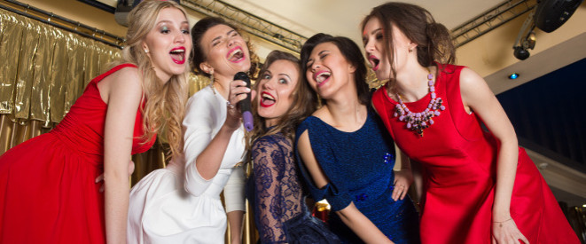 Gruppe junger Frauen in Abendgarderobe singt inbrünstig in ein Mikrophon