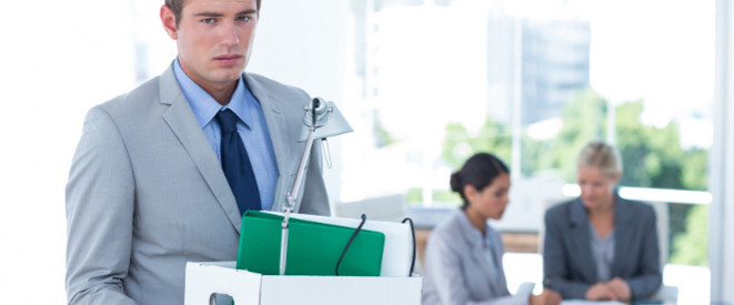 Versetzung: Traurig schauender Mann im Anzug hält Pappkarton mit seinem Büro-Zubehör 