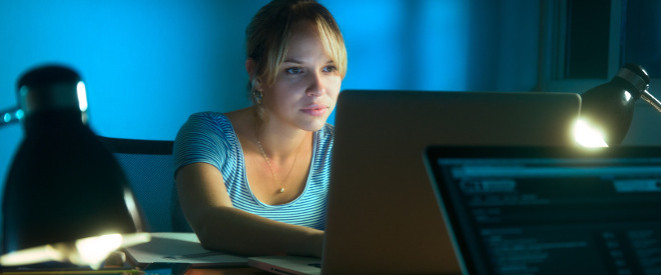 blonde Frau sitzt in abgedunkeltem Raum vor dem Computer