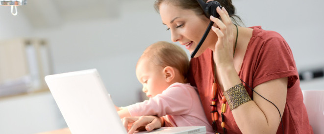 Arbeiten während der Elternzeit: Mutter mit Headset arbeitet mit Kleinkind auf dem Schoß am Computer