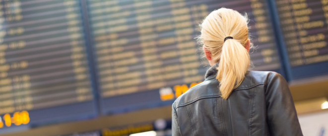 Blonde Touristin steht bei Flugbegleiter-Streik vor der Anzeigetafel am Flughafen
