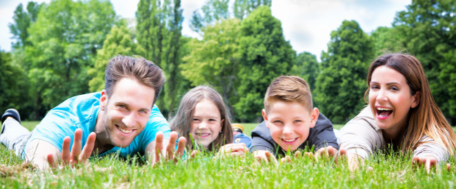 Eltern mit kleinen Kindern liegen im Gras und lächeln in die Kamera