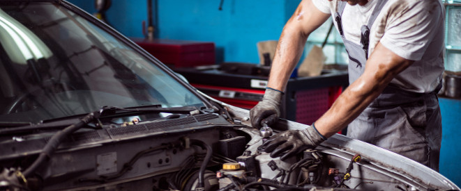 Mechaniker arbeitet bei offener Motorhaube an einem Auto