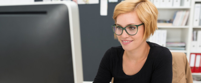 Ergonomie am Arbeitsplatz: junge Frau mit Brille und kurzen Haaren sitzt vor dem Computer-Bildschirm