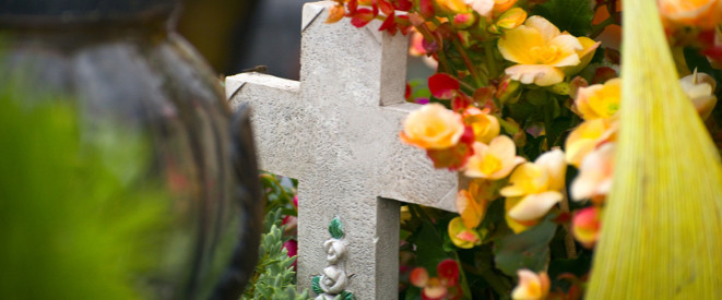 Grabgestaltung: Ein graues Kreuz umrankt von Blumen.