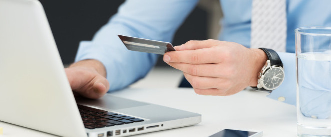 Phishing: Ein Mann sitzt vor einem Laptop und hält eine Kreditkarte in der Hand.