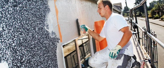 Sanierungskosten: Ein Mann verputzt eine Fassade.