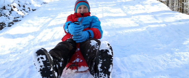 Schlitten und Snowboard fahren: Ein Kind sitzt auf einem Schlitten: