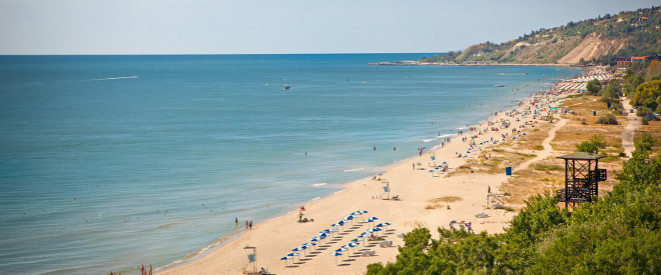 Blaues Meer trifft auf gelben Sandstrand, an dem Urlauber baden.