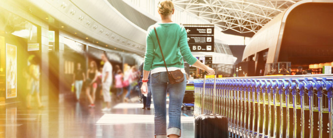 Flugbuchung: Ticketpreis darf sofort abgebucht werden. Eine Frau geht mit einem Koffer auf Rollen durch ein Flughafen-Terminal.