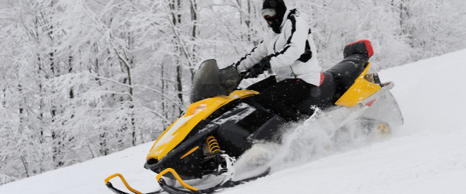 Eine Persone fährt auf einem gelben Schneemobil durch eine verschneite Landschaft.
